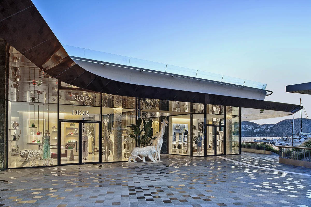 Illuminated Dior shopfront beside the marina promenade at dusk.