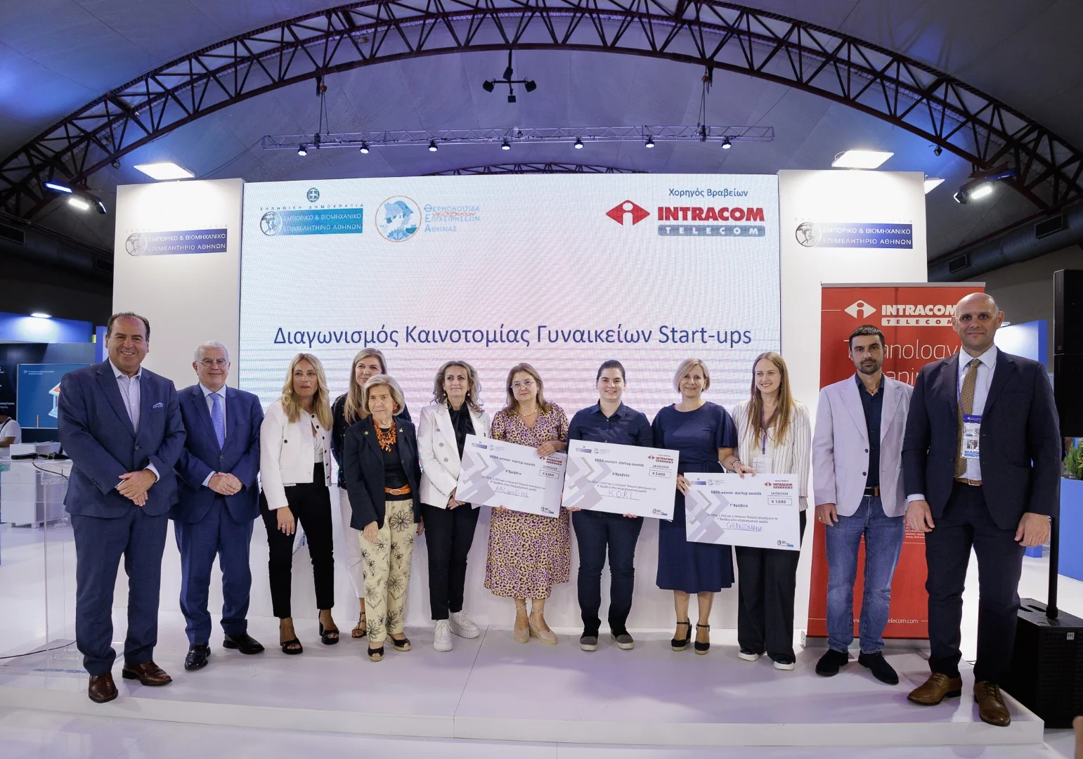 Group at the THEA women’s startup competition awards, holding prize certificates in front of the event screen.