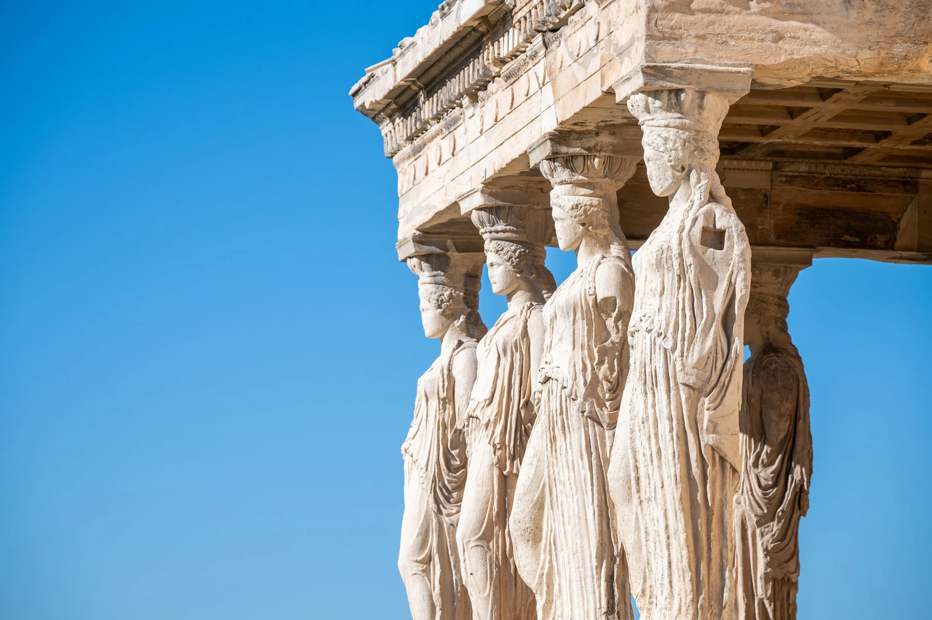 Stone Caryatids supporting the Erechtheion porch against a clear blue sky.